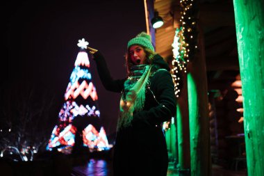 Noel ağacı yıldızına dokunmak - Genç çekici kızıl saçlı kız lunaparkta takılıyor parlak renkli çekimler ve kurulum geçmişiyle