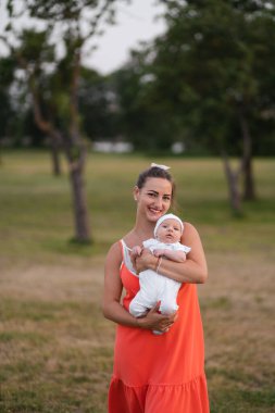 Genç anne tutan ve parlak kırmızı elbise giyen şehir parkı ayakta onun bebek erkek çocuk ile oynarken - Oğlu beyaz şapka giyer - Aile değerleri sıcak renk yaz sahnesi el