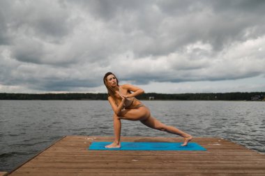 Bulutlu gölde mini bikinili yoga egzersizleri yapan sıska bir kadın - Yoga meditasyonu ve sağlık yaşam tarzı kavramı - Avrupa Doğu Letonya Riga