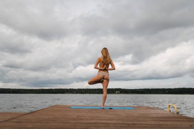Bulutlu gölde mini bikinili yoga egzersizleri yapan sıska bir kadın - Yoga meditasyonu ve sağlık yaşam tarzı kavramı - Avrupa Doğu Letonya Riga