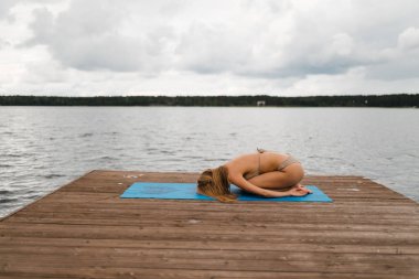 Bulutlu gölde mini bikinili yoga egzersizleri yapan sıska bir kadın - Yoga meditasyonu ve sağlık yaşam tarzı kavramı - Avrupa Doğu Letonya Riga