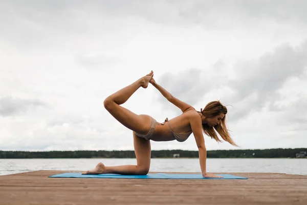 Fitte schlanke Frau praktiziert Yoga-Übungen im Mini-Badeanzug-Bikini am wolkenverhangenen See - Yoga-Meditation und Wellness-Lifestylekonzept - Europäisches Ostlettland riga — Stockfoto