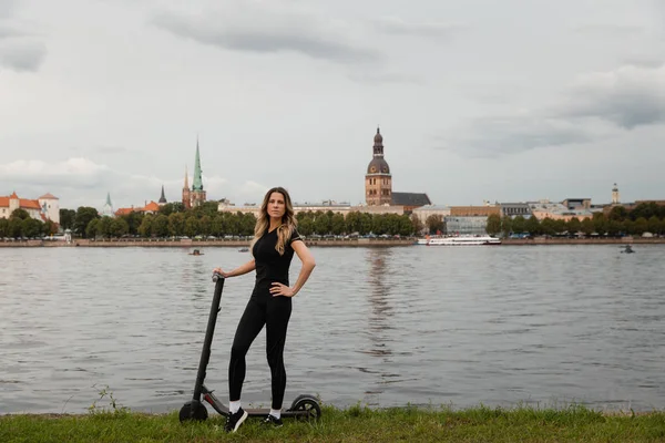 Fit Woman by electric scooter with a river city background - Shot of Modern transport gadget en populair futuristisch apparaat onder jongeren - Oost-Europa Letland Riga — Stockfoto