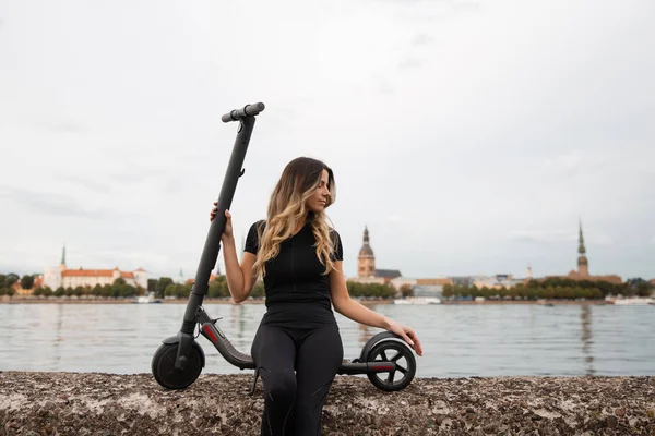 Fit Woman by electric scooter with a river city background - Shot of Modern transport gadget en populair futuristisch apparaat onder jongeren - Oost-Europa Letland Riga — Stockfoto