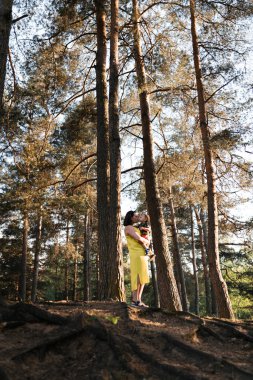 Orman ahşap bebek çocuk çocuk oynarken Anne yürüyüş - Yeşil elbiseli genç anne ve yeşil bir parkta eğlenen bebeği - Mutlu gülümseyen insanlar