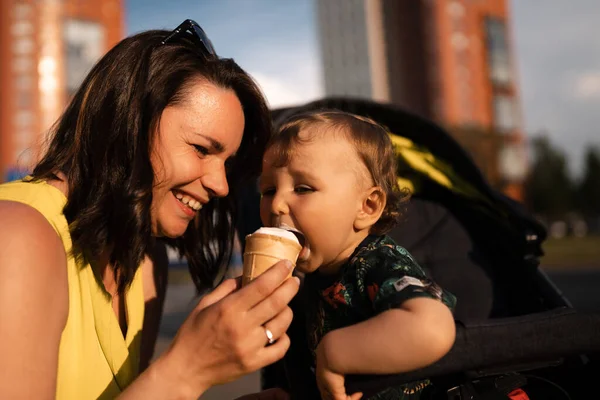 Anne besleme bebek çocuk çocuk dondurma - Genç anne ve bebeği beyaz vanilya kremsi tatlı yemek - Bir bebek arabası bebek arabası oturur - Kafkas aile 1 yaşında