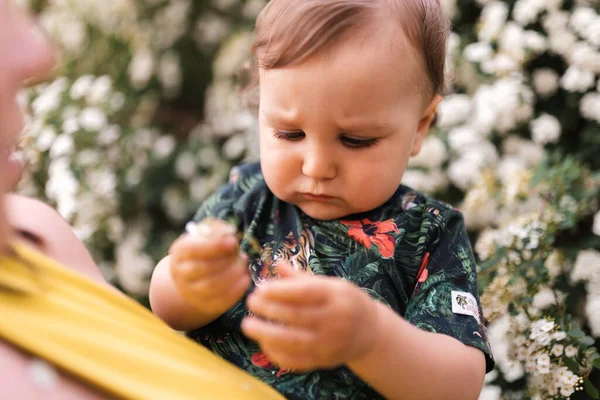 Madre jugando y hablando con el bebé niño con el árbol de flores en flor en el fondo - Madre joven en vestido verde y su bebé en un parque verde divirtiéndose - Personas sonrientes felices —  Fotos de Stock