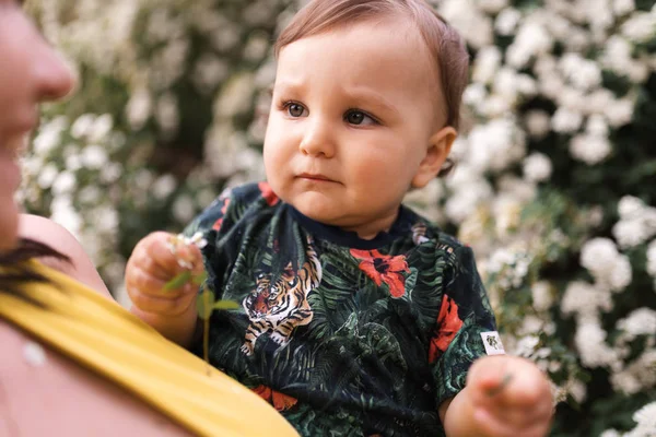 Mãe brincando e conversando com bebê menino com flor árvore florescente no fundo - Mãe jovem em vestido verde e seu bebê em um parque verde se divertindo - Pessoas sorridentes felizes — Fotografia de Stock