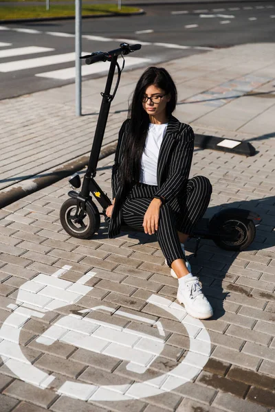 Zakelijke vrouw zit op elektrische scooter dragen pak op parkeerplaats opladen - Emissie gratis eco-vriendelijk vervoer — Stockfoto