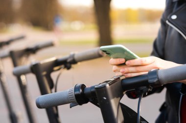 Dişi eller yakın görüş. Kadın telefonu tutuyor ve elektrikli scooter kiralıyor.