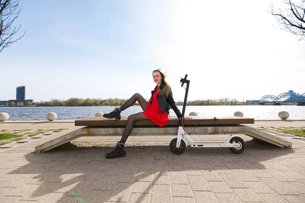 Mooie jonge blonde vrouw zit op bank met witte elektrische scooter — Stockfoto