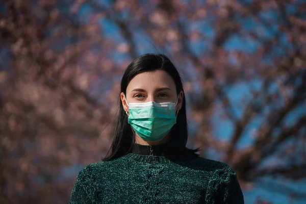 Triste jovem mulher usa máscara cirúrgica com sakura no fundo — Fotografia de Stock