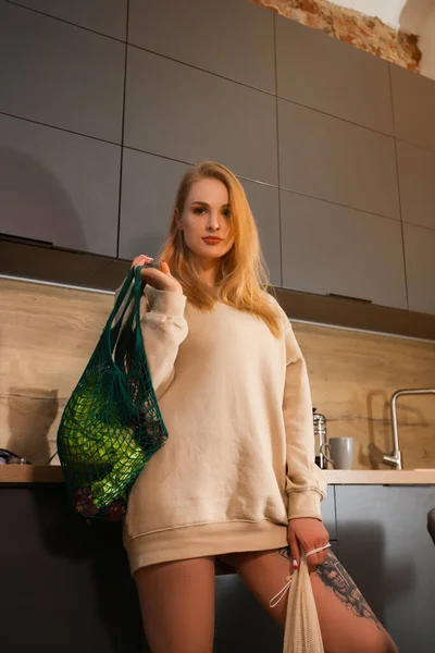 Vrouw met grocey tassen staat in de keuken — Stockfoto