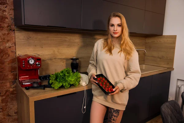 Woman with grocey bag on kitchen table holds cherry tomatoes — Stock Photo, Image