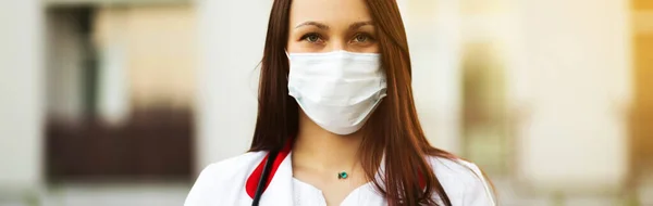 Młoda kobieta lekarz w masce chirurgicznej i słuchawki na zewnątrz baner — Zdjęcie stockowe