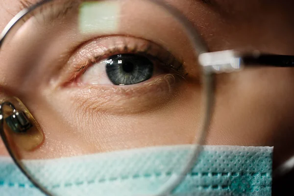 Médico femenino lleva máscara médica y te mira a través de gafas — Foto de Stock