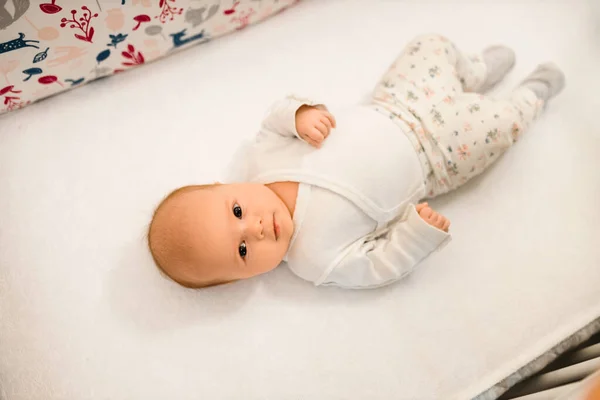 Little female toddler lies in crib, smiles and show tongue — Stock Photo, Image