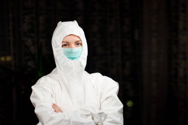 Koruyucu tıbbi giysi ve cerrahi maske takmış kadın doktor sana bakıyor.