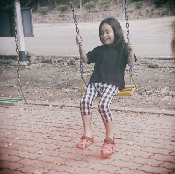 Happy child sitting swinging on swing at outdoor park — Stock Photo, Image