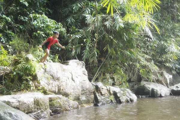 Funny child jumping high into waterfall. kids water sport activity.