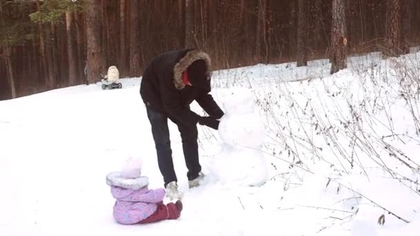 子供を持つ若い父親は雪だるまを作ります。冬の休日のためのストリートエンターテイメント. — ストック動画