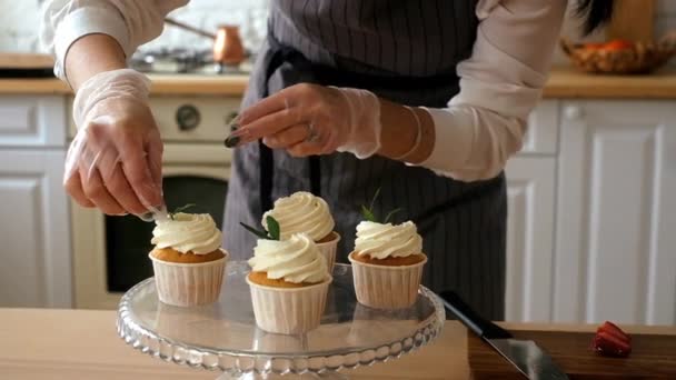 Жінка-кондитер прикрашає кекси. На кухні — стокове відео