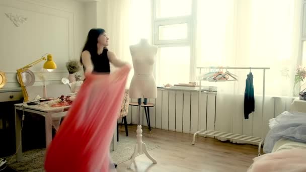 Diseñadora femenina trabajando en un vestido rosa transparente en su luminoso estudio. Mujer joven viste un vestido en un maniquí blanco — Vídeos de Stock