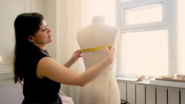 Terzi, profesyonel moda tasarımcısı. Bir mankeni metreyle ölçer. Dikiş stüdyosu. Yarım boy, kadın 30-40 yaşlarında.