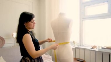 Terzi, profesyonel moda tasarımcısı. Bir mankeni metreyle ölçer. Dikiş stüdyosu. Yarım boy, kadın 30-40 yaşlarında.