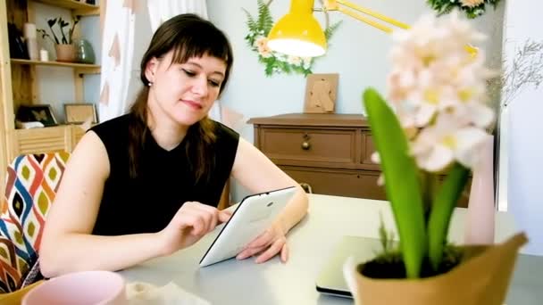 Giovane donna utilizza un tablet mentre si rilassa a casa a tavola. Vista a mezza lunghezza, femmina 30-40 anni  . — Video Stock