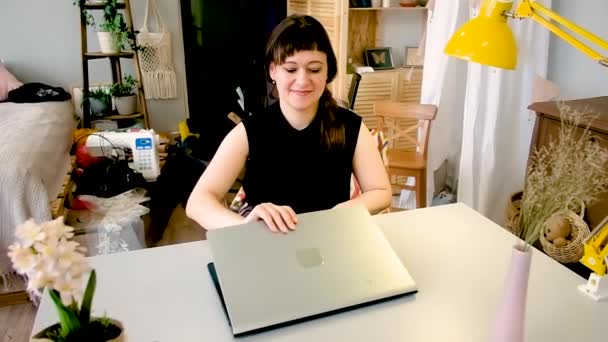 Vrouw zit aan een tafel werkend aan een laptop. Freelance, thuis werken, buiten het kantoor werken. Afstandsonderwijs. Moderne technologieën en communicatie. vrouw 30-40 jaar . — Stockvideo