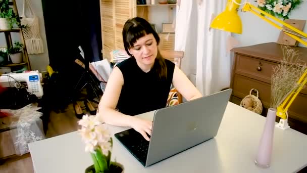 Mulher senta-se a uma mesa trabalhando em um laptop. Freelance, trabalho em casa, trabalho fora do escritório. Educação à distância. Tecnologias e comunicações modernas. mulher 30-40 anos  . — Vídeo de Stock