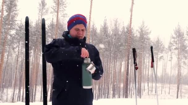 Langläufer trinkt im Stillstand aus einer Thermoskanne. Wintersport. Aktive Erholung im Winter. Skistrecke. junger Mann 20-25 Jahre — Stockvideo