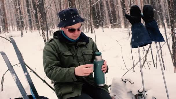 Längdskidåkare dricker från en termos vid ett stopp. Vintersport. Aktiv vila på vintern. Skidspår. ung man 20-25 år — Stockvideo