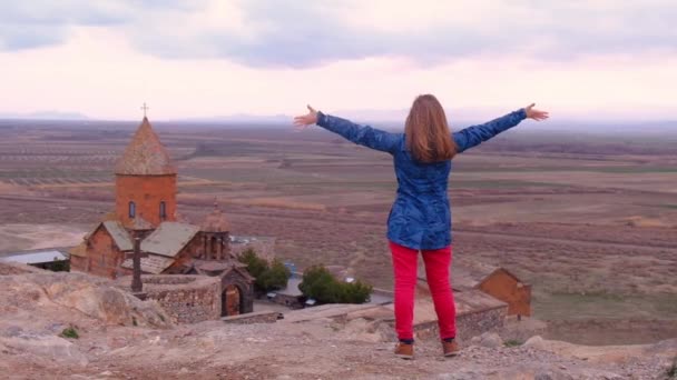 Όμορφη γυναίκα κουνάει τα χέρια της στο φόντο της εκκλησίας Khor Virap στην Αρμενία. Ταξιδέψτε σε όλο τον κόσμο. Ελεύθερη κυκλοφορία των προσώπων — Αρχείο Βίντεο
