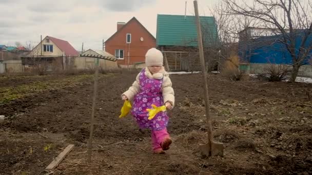 Kleines niedliches, fröhliches Gärtnermädchen, das mit Gummihandschuhen in der Hütte tanzt. Beginn der Feldarbeit — Stockvideo