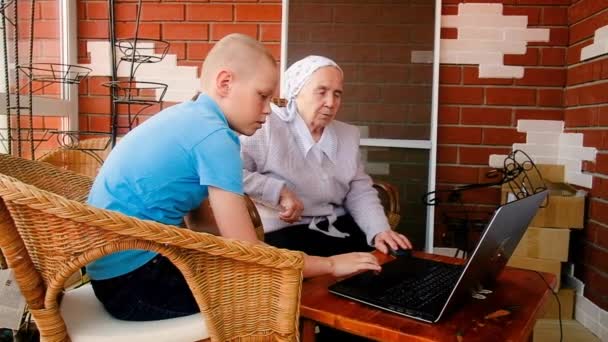 Barnbarn lär 80-åriga mormor att arbeta med en smartphone. Leka med en smartphone. Gör inköp på nätet. är fotograferade. på verandan i huset. Kommunicera på Internet — Stockvideo