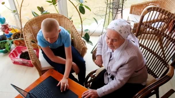 Nietos enseñan a 80 años de edad abuela a trabajar en un teléfono inteligente. jugando con un smartphone. Hacer compras en línea. son fotografiados. en la veranda de la casa. Comunicarse en Internet — Vídeo de stock