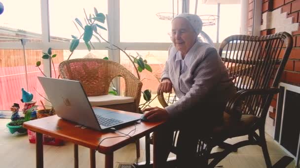 Oma werkt op een laptop. communiceert online met kleinkinderen — Stockvideo