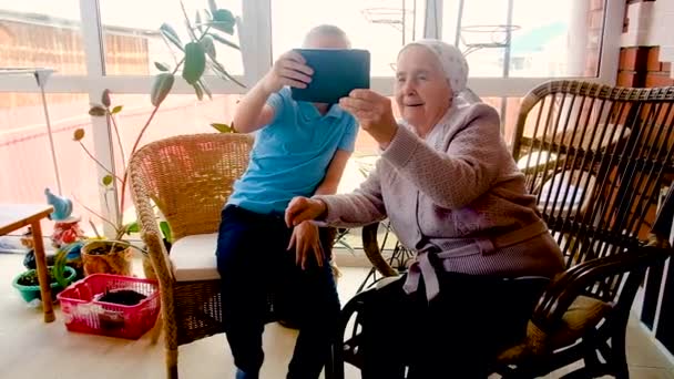 El nieto le muestra a la abuela cómo trabajar en un gadget.play en la tableta . — Vídeo de stock