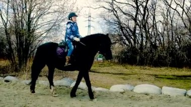 Genç kız, toprak yolda siyah zarif bir ata binen at jokeyi.