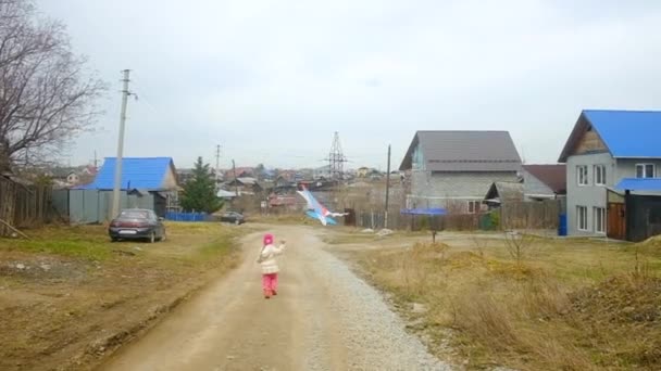 Piccola ragazza carina con un aquilone al cottage. Correndo lungo la strada tra le case. infanzia spensierata divertimento — Video Stock