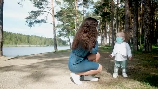 Ung mor och liten dotter i skyddsmasker för en promenad i parken. — Stockvideo