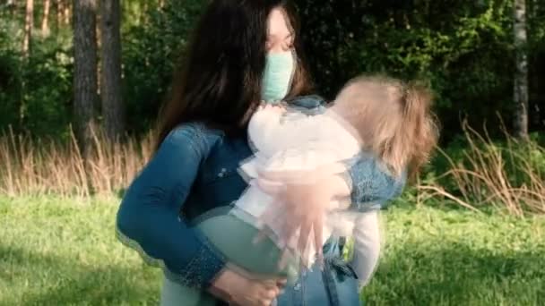 Νεαρή μητέρα και μικρή κόρη με προστατευτικές μάσκες για μια βόλτα στο πάρκο. — Αρχείο Βίντεο