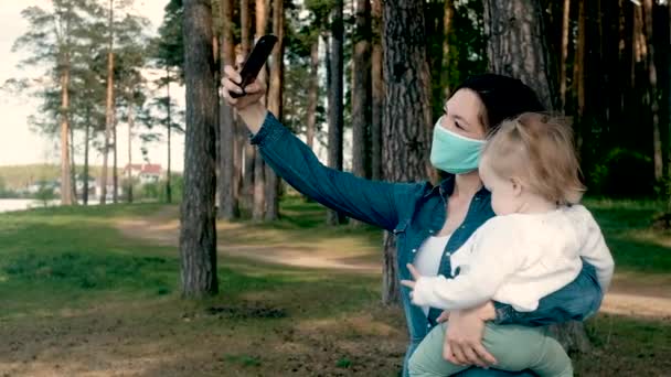 Junge Mutter und kleine Tochter in Schutzmasken für einen Spaziergang im Park. — Stockvideo