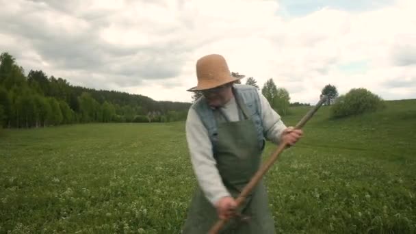 Stark man 60-65 år gammal med lie gräsklippare grönt gräs på fältet. — Stockvideo