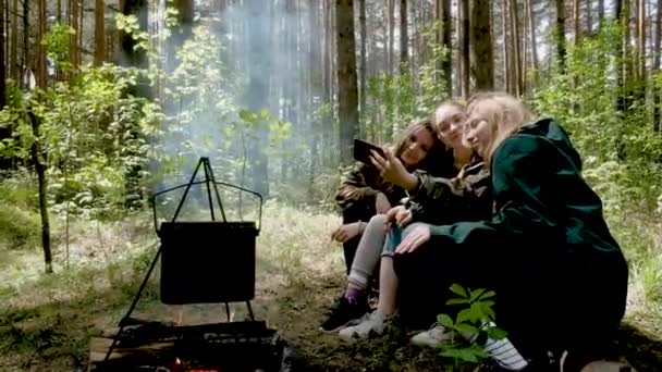 Молоді дівчата сидять біля багаття в лісі. Смажені ковбаски під час походу в кемпінг. Вони роблять чай. Активний спосіб життя в природі. літня поїздка. Концепція дружби та дозвілля — стокове відео