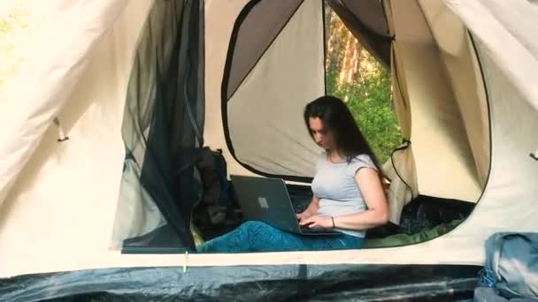 Giovane turista donna è seduto in una tenda e lavorare su un computer . — Video Stock