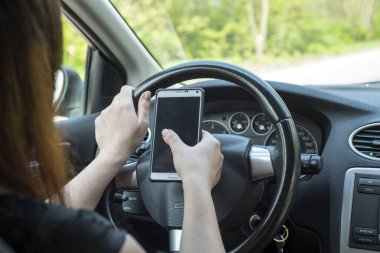 kadın sürücü sürüş sırasında elinde cep telefonu ile.