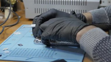 Adam atölyede bozuk akıllı telefonu tamir ediyor.